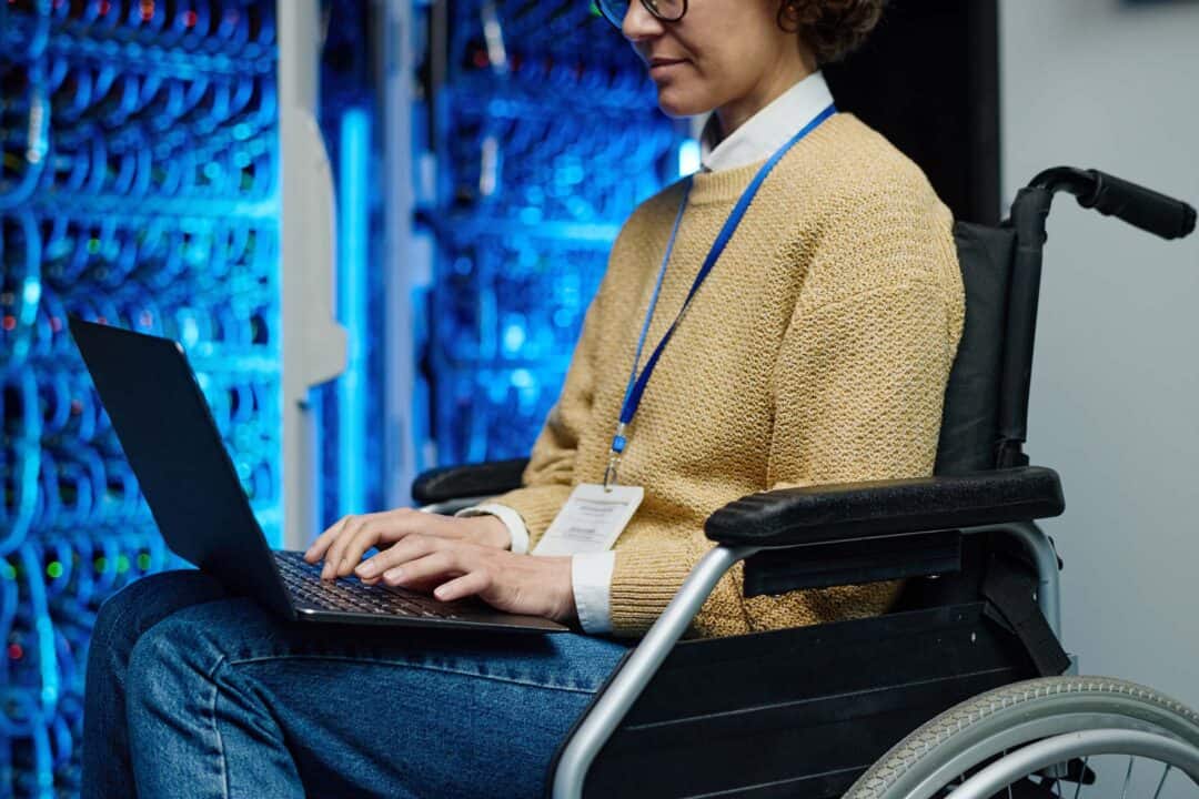 Une informaticienne dans une salle de serveurs utilisant son ordinateur portable depuis son fauteuil roulant